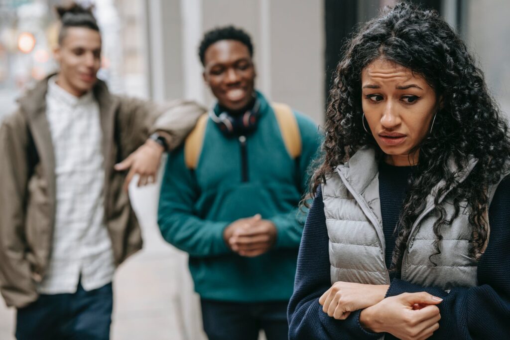 diverse multiracial male students intimidating ethnic female classmate on street